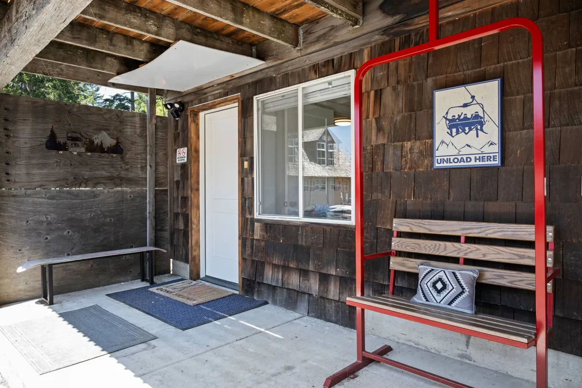 This interior image depicts a red bench situated by a window, with an 'Unload Here' sign prominently displayed. The area features hooks and a welcoming spot to sit and remove shoes or set down gear, giving the feeling of a practical entry or mudroom zone.
