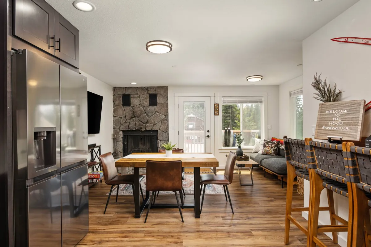 A warm, welcoming interior scene featuring a stone fireplace, large dining table, and bright window views. This space radiates comfort with cozy gathering opportunities after a day of outdoor exploration with pets and family.