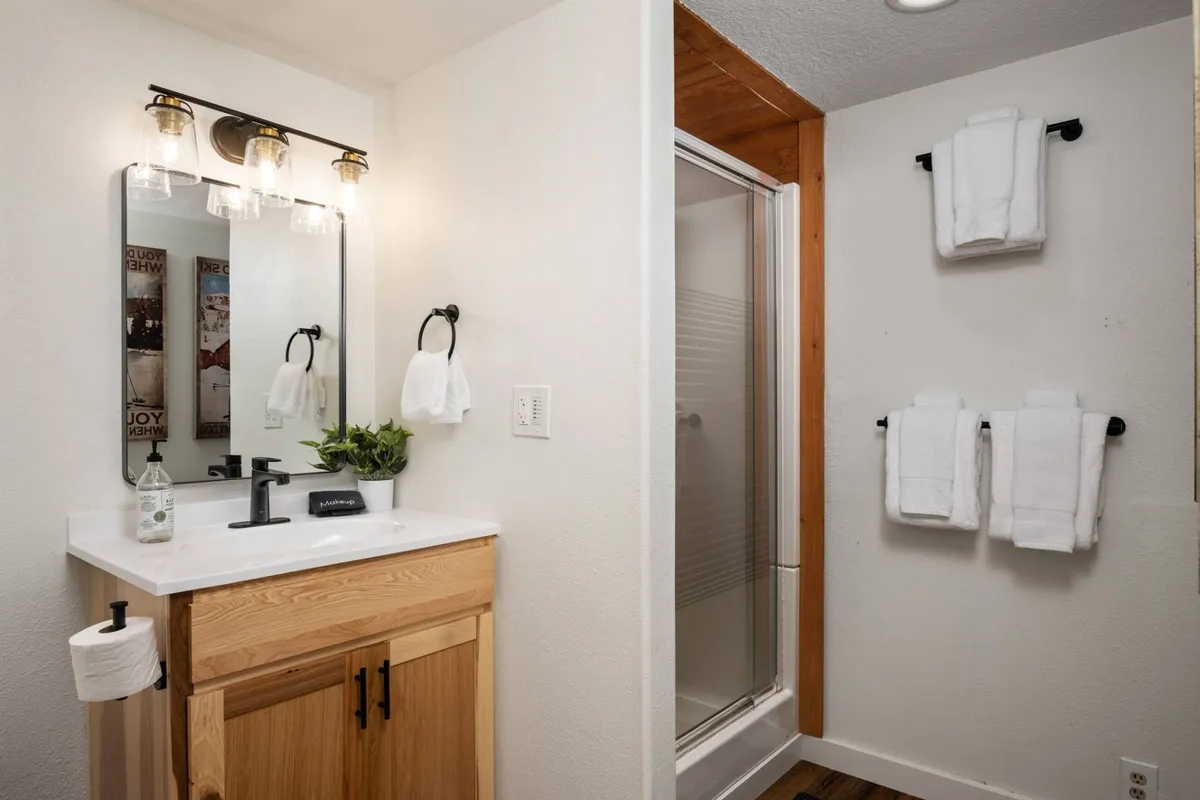A bright and modern en-suite bathroom with a vanity and mirror, a spacious shower area with glass doors, and an organized towel rack. The space is clean, fresh, and welcoming, ideal for self-care and relaxation.