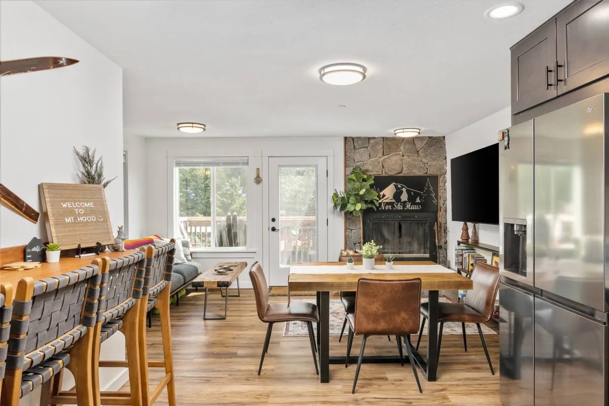 A welcoming communal area featuring a dining table with barstools, a fireplace, and sliding glass doors opening to the outside. The scene is set for family dinners, storytelling by the fireplace, and enjoying the view—perfect for both holiday feasts and relaxed mornings.