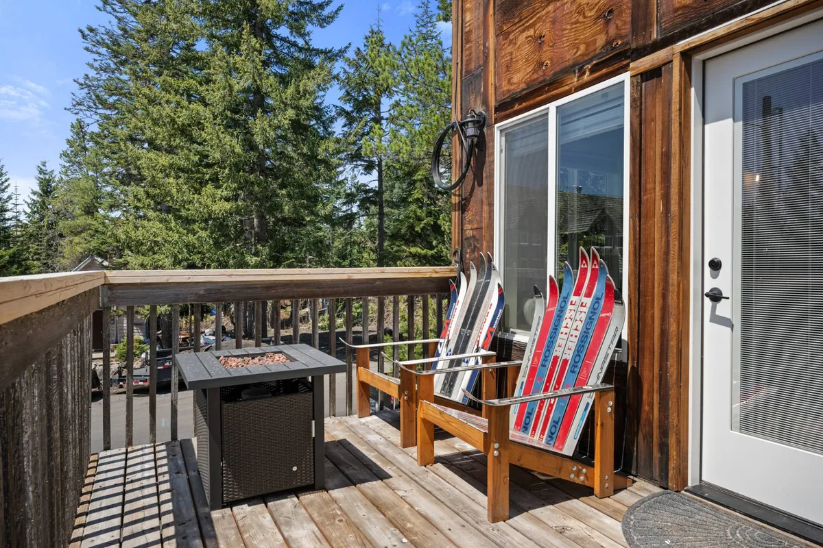 A cozy outdoor deck area featuring wooden chairs crafted from skis, arranged around a central fire pit. Tall pine trees create a natural backdrop, and the warm glow from the fire invites relaxation and conversation. The setting is ideal for après-ski gatherings or unwinding after a day of adventure.