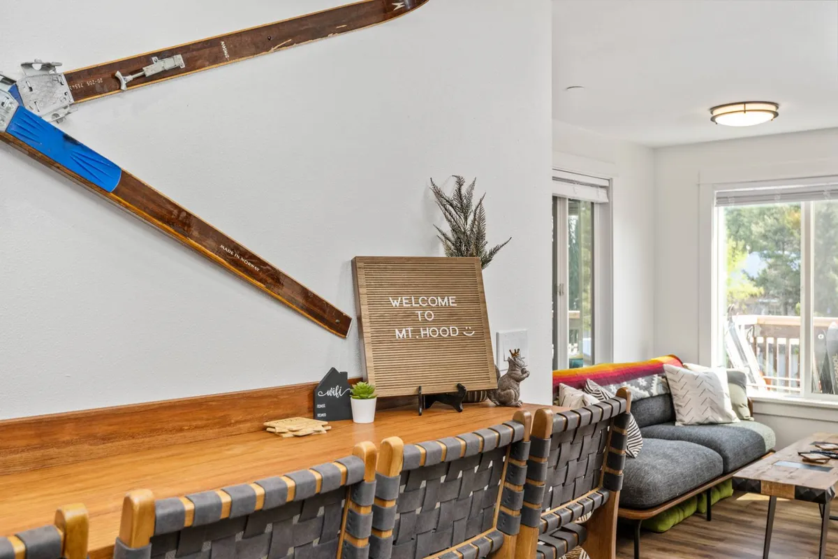 A cozy corner with wall-mounted skis, a welcome sign, inviting seating, and a plant on the counter. The scene evokes relaxation after outdoor activities, with decor that echoes the Mt. Hood skiing and trail environment.