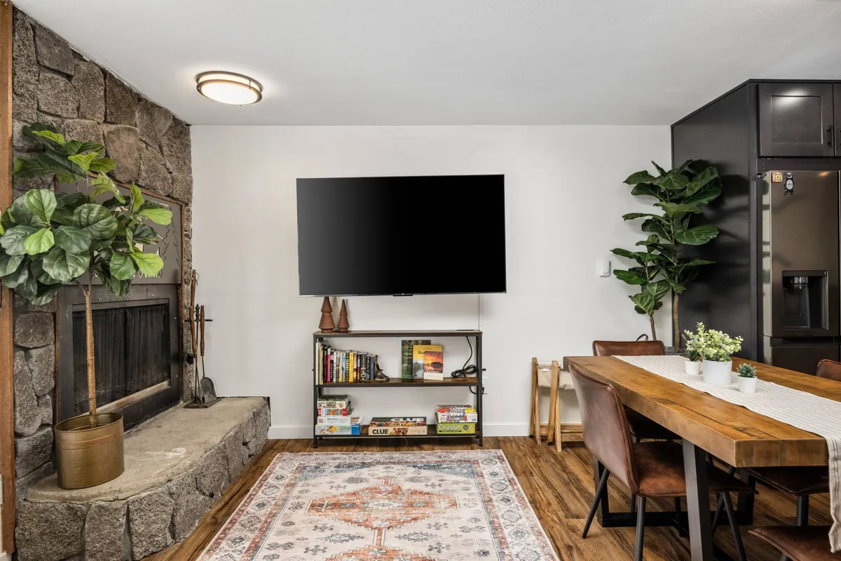 This image centers on a welcoming living area with a stone fireplace, a large TV, and a dining table. The cozy mood and visible features—perfect for family gatherings, movie nights, and shared meals—echo the section’s mentions of plush living areas and group relaxation. The fire and ample seating evoke warmth and comfort after mountain adventures.