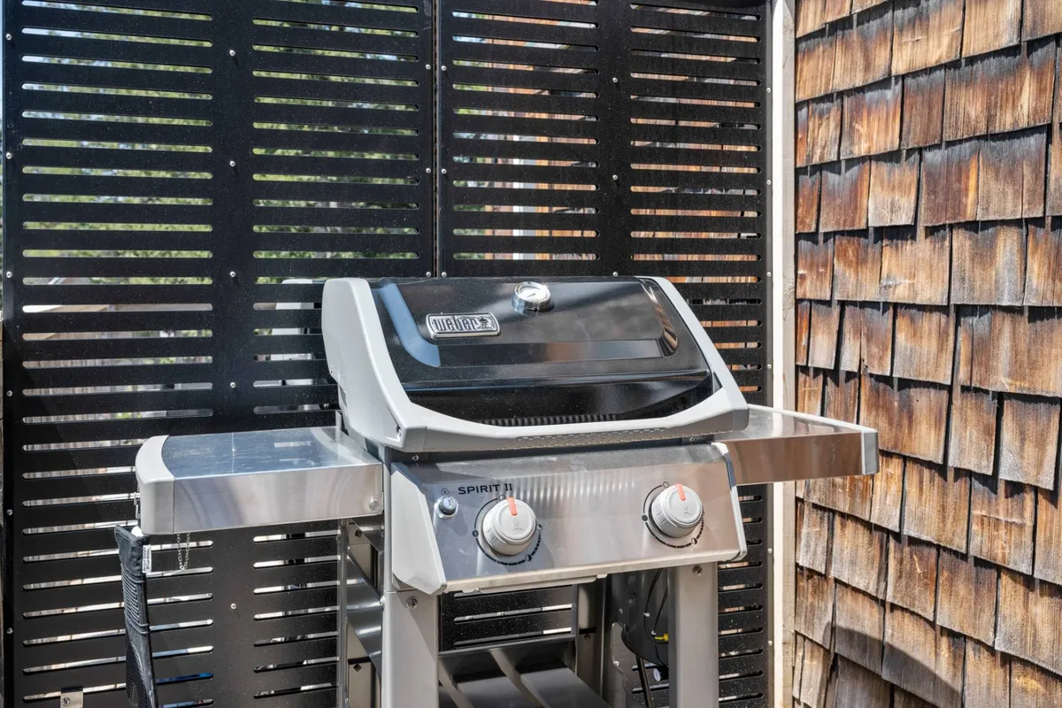An inviting outdoor area featuring a grill set against wooden wall panels, suggesting a private deck or patio perfect for après-adventure relaxation and group barbecues. The scene is casual, warm, and ready for gatherings after a day outside.